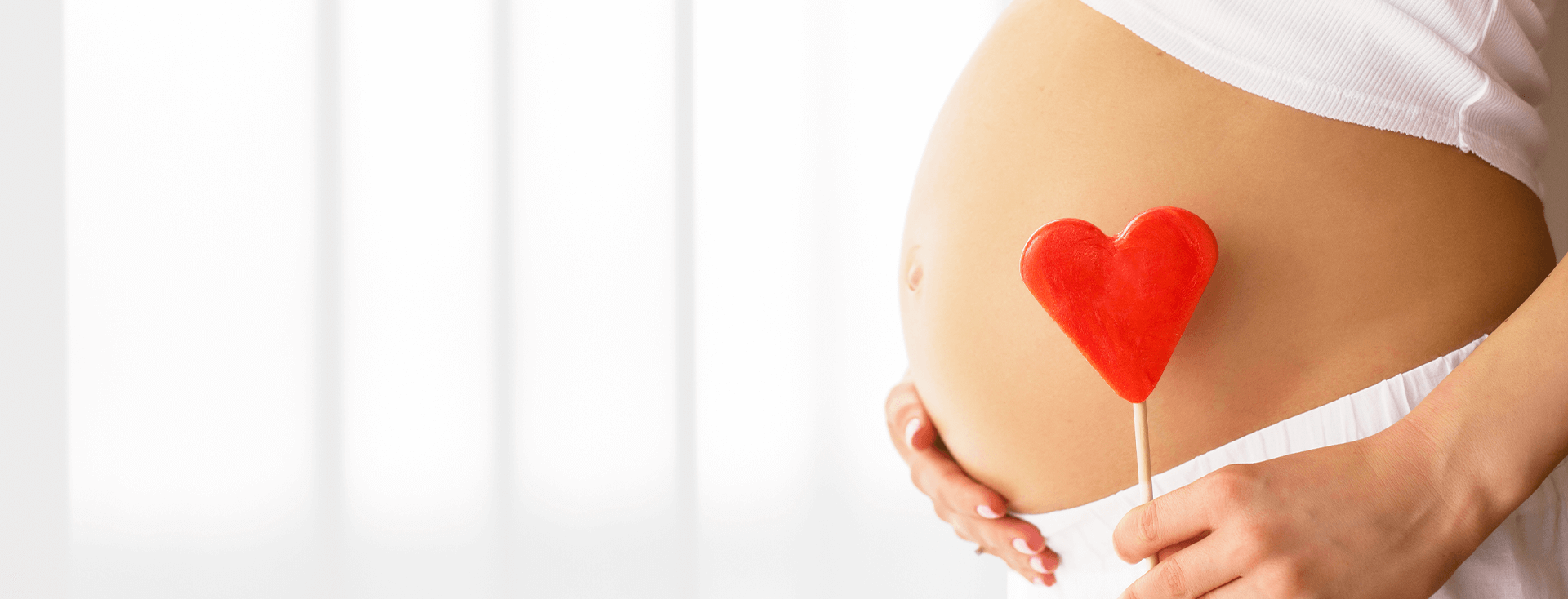 barriga de gestante segurando um enfeite de coração para representar a importância da suplementação na gravidez