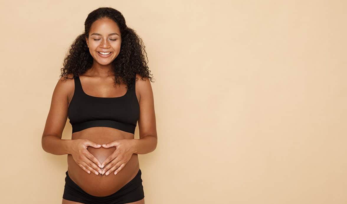 mulher grávida com as mãos na barriga, formando um coração