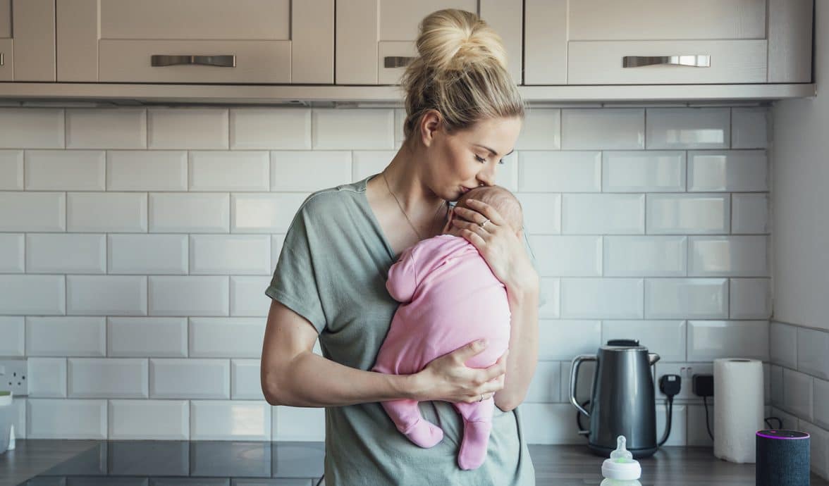 jovem mãe segura bebê contra o peito, com ternura, na cozinha