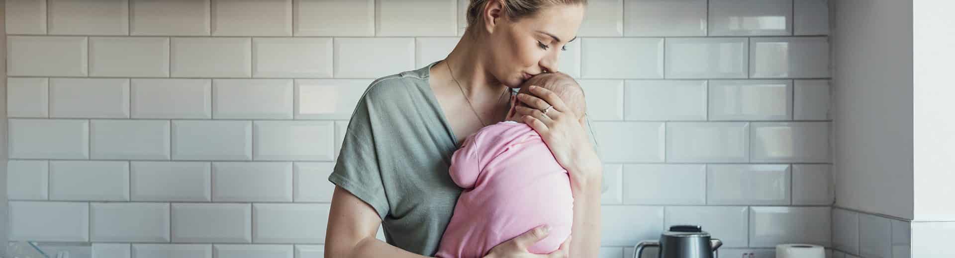 jovem mãe segura bebê contra o peito, com ternura, na cozinha
