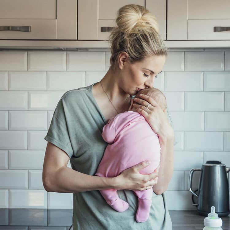 jovem mãe segura bebê contra o peito, com ternura, na cozinha