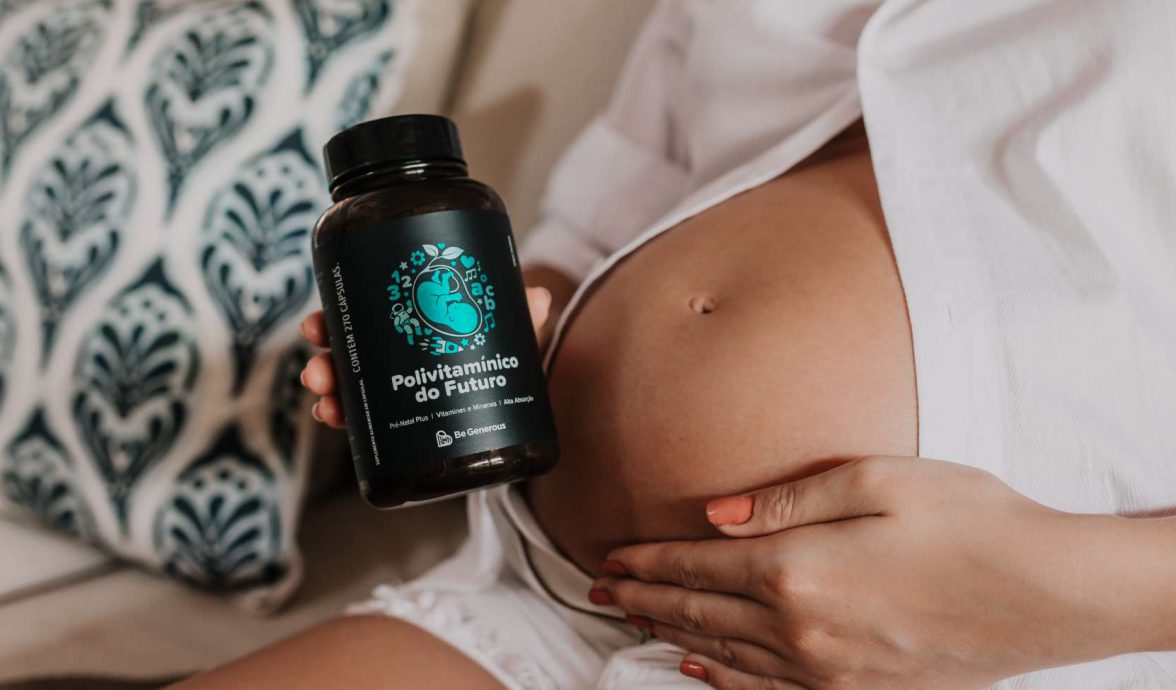 Imagem de uma mulher com uma mão na barriga e a outra segurando vitaminas para gestantes.