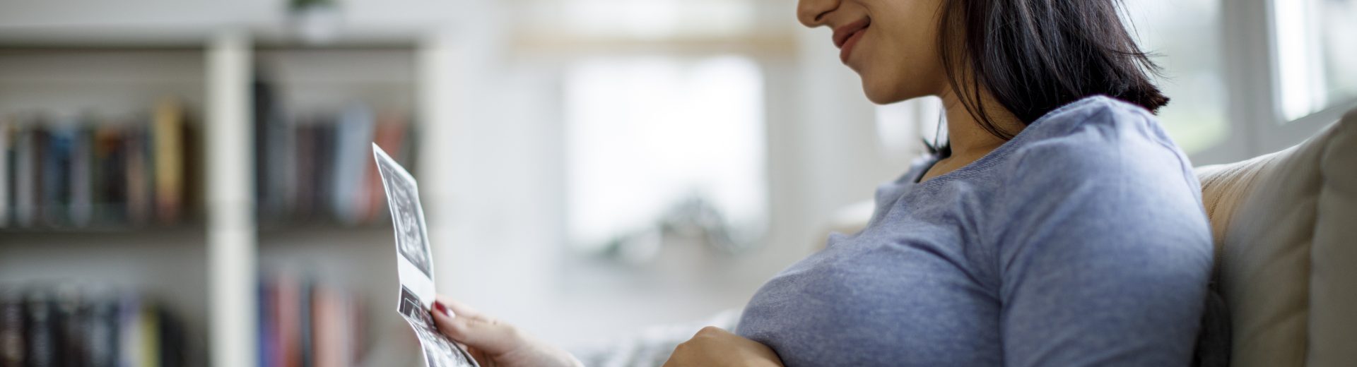 Gestante sentada com a mão sobre a barriga, olhando imagens de ultrassom do bebê, um dos exames obrigatórios no pré-natal.