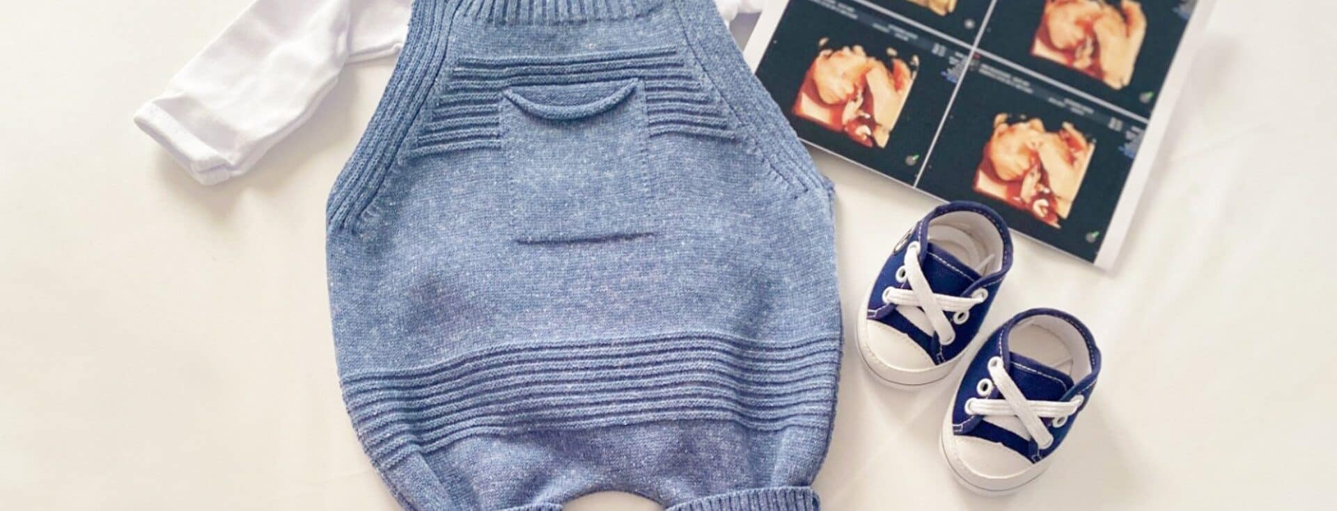 Imagem com uma roupinha de bebê azul, sapatinhos em azul e branco e uma imagem de ultrassom. Os elementos estão espalhados em cima de um fundo branco.