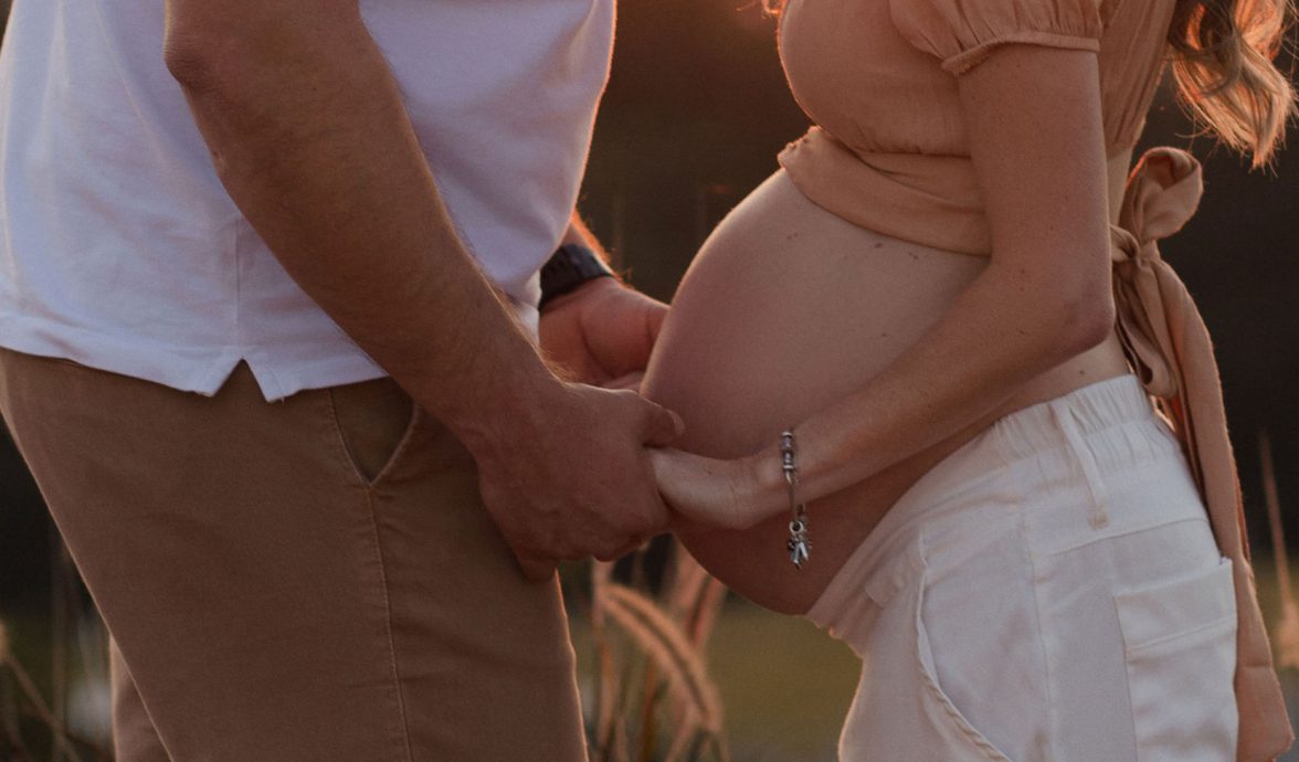 Homem e mulher grávida, um de frente para o outro, de mãos dadas.