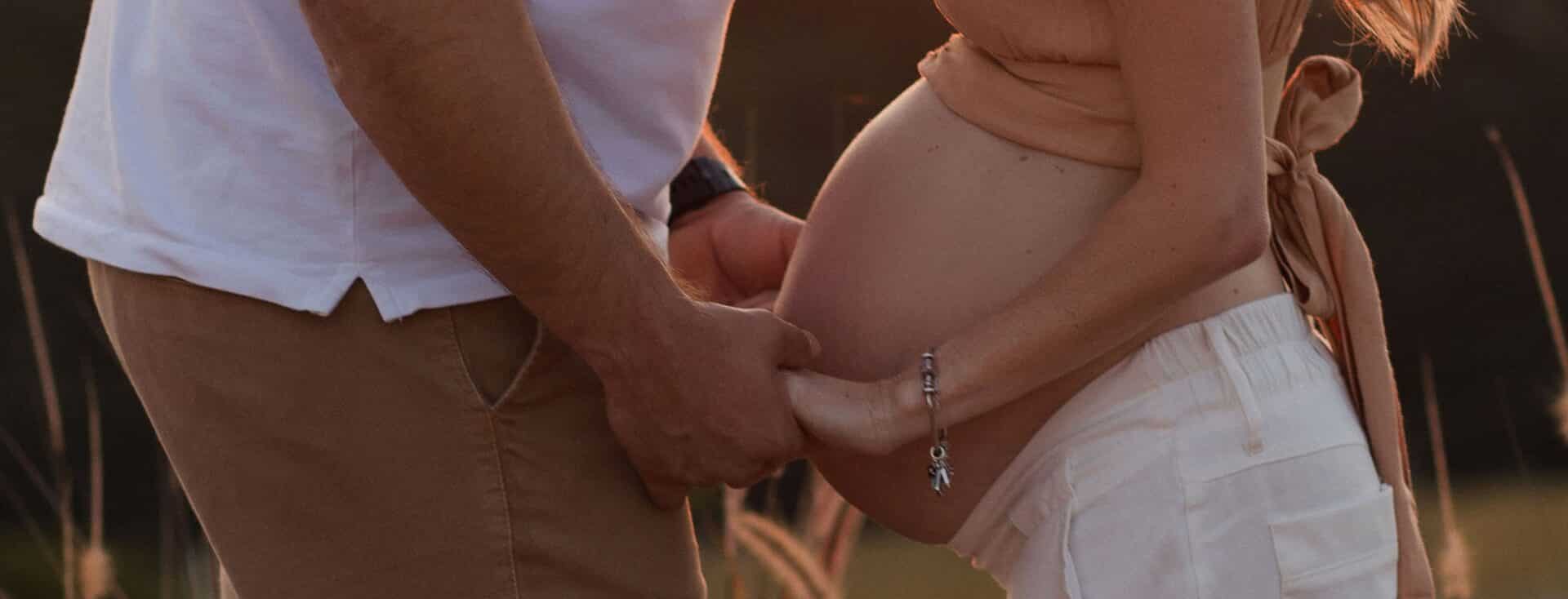 Homem e mulher grávida, um de frente para o outro, de mãos dadas.