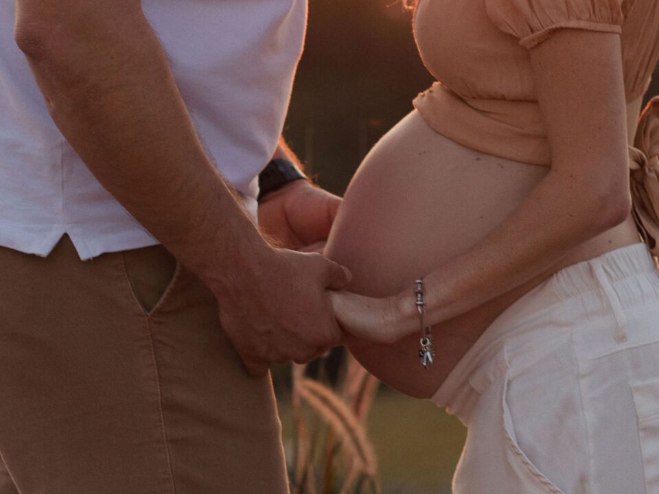 Homem e mulher grávida, um de frente para o outro, de mãos dadas.
