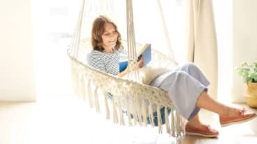 Imagem de uma mulher sentada em um balanço, lendo um livro e sorrindo em um momento de autocuidado materno.