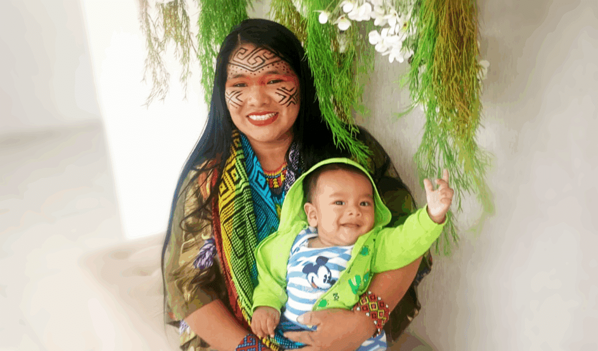 Imagem da indígena Txima Inani Bake com seu bebê Be Generous, Arlis Siã, no colo. Ambos estão felizes e saudáveis.